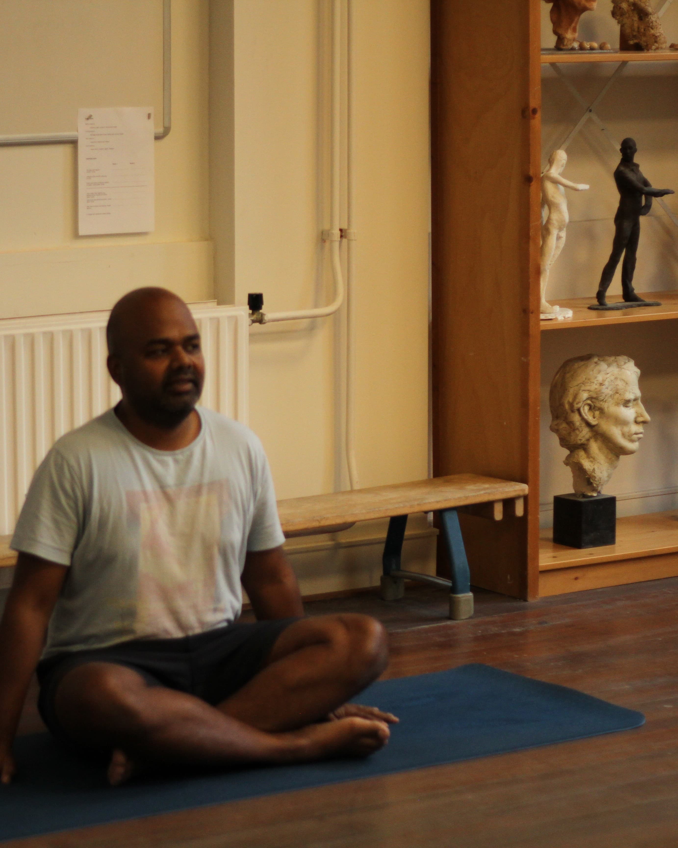 Karthikeyan seated in a yoga posture beside the sculpture shelves at Figura
